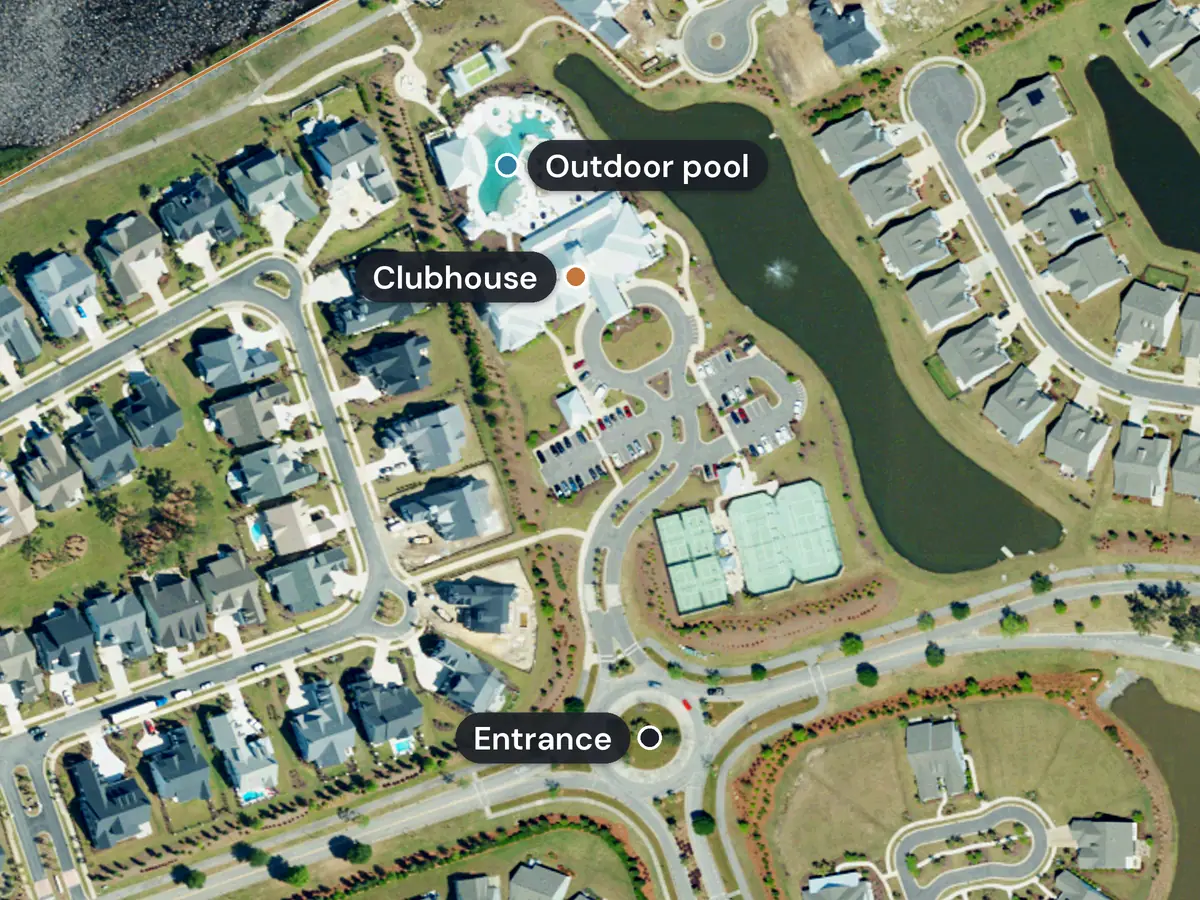 The Del Webb at Grande Dunes clubhouse from above, with its large outdoor pool, parking, courts and a pond beside it, and the entrance marked