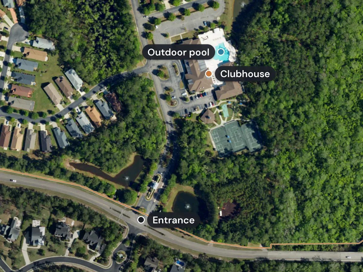 The Seasons at Prince Creek West clubhouse from above, with its outdoor pool, parking lot and tennis courts among the trees, and the entrance road marked
