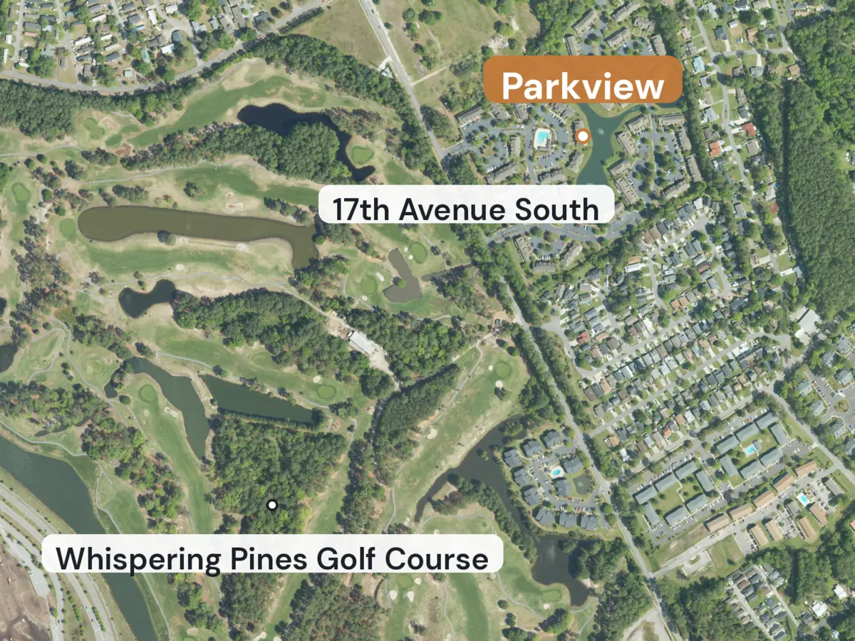 Aerial view of townhomes around a pond beside a road, with golf course fairways and ponds to the southwest, with labels