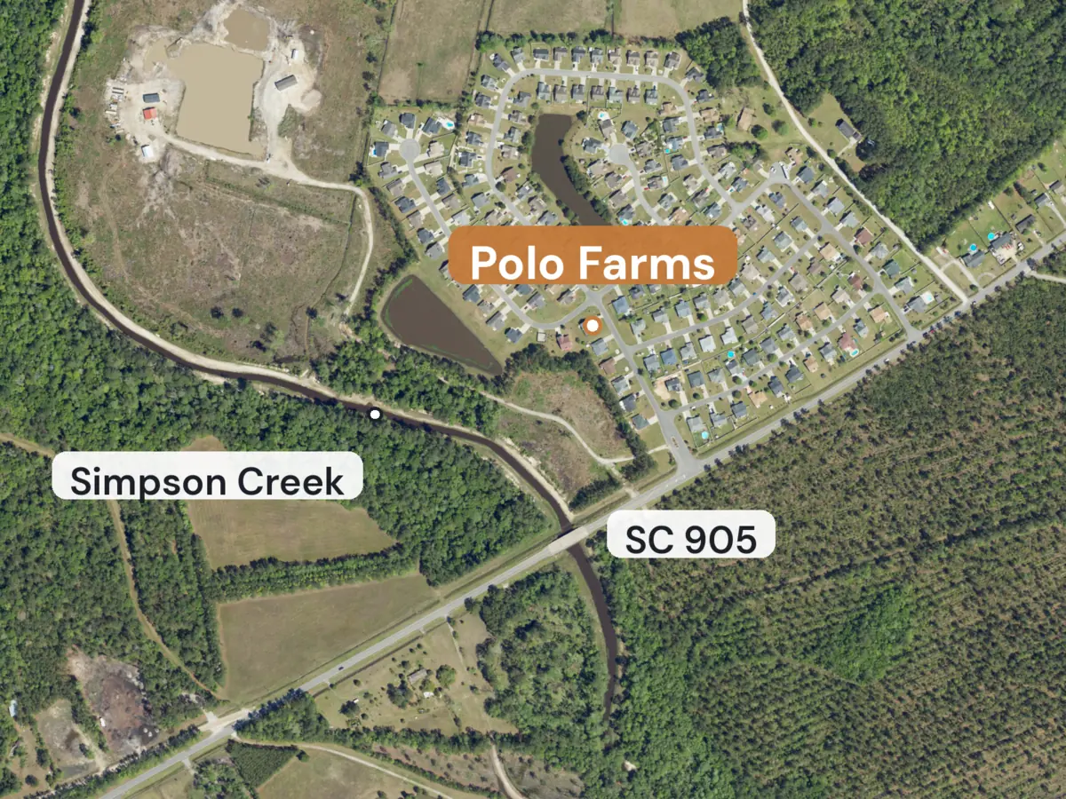 Aerial view of a neighborhood of houses with fenced yards and two ponds, a creek curving past it and a highway, with labels for Polo Farms, SC 905 and Simpson Creek