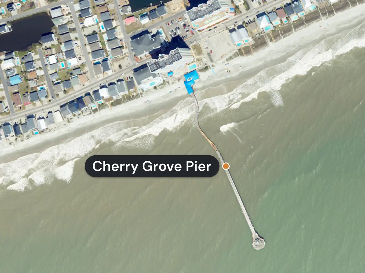Cherry Grove from above: a long wooden pier labelled Cherry Grove Pier runs from a blue building on the beach out past the waves, with rows of beach houses behind the sand