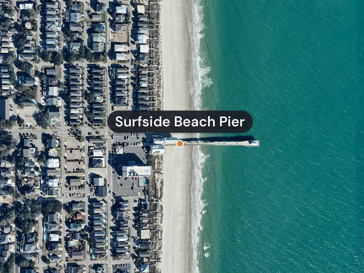 Surfside Beach from the air: a long pier labelled Surfside Beach Pier runs from the beach into a green ocean, with rows of houses on the streets behind the sand