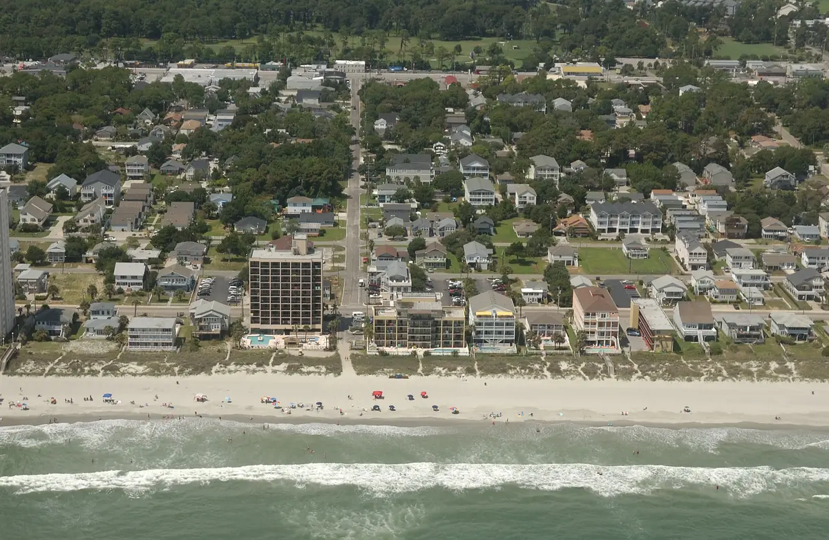 Streets of two-story beach houses among trees behind the oceanfront at Crescent Beach in North Myrtle Beach, seen from a plane over the ocean
