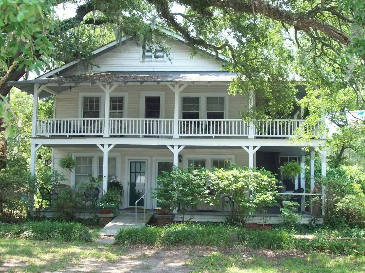 A two-story white wood house with long porches on both floors, shaded by big oak trees with Spanish moss, on Broadway Street in downtown Myrtle Beach